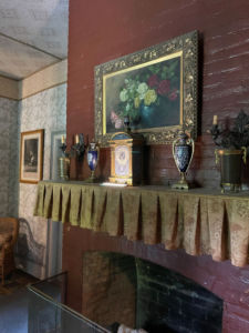 fireplace with mantle shelf objects including a metal clock showing the time of approximately 8:07